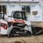 Bobcat Construction Equipment Compact Truck Loader with Bucket Attachment plowing dirt at construction site for a new building. Bobcat Construction Equipment Compact Truck Loader with Bucket Attachment plowing dirt at construction site for a new building.