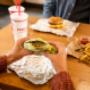 A customer's hands hold a Five Guys lettuce wrap at a dining room table inside a Five Guys restaurant. A customer's hands hold a Five Guys lettuce wrap at a dining room table inside a Five Guys restaurant.