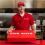 A Five Guys employee holds the red Five Guys catering box at the counter. A Five Guys employee holds the red Five Guys catering box at the counter.
