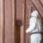 A man in a white suit installs Insulthane Extreme insulation in an attic, carefully fitting rolls between rafters. The home's energy efficiency is improved as gaps are eliminated. A man in a white suit installs Insulthane Extreme insulation in an attic, carefully fitting rolls between rafters. The home's energy efficiency is improved as gaps are eliminated.