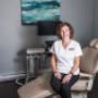 ID for accessibility: Tobi Stuckless RDH is sat on a beige dental chair in a treatment room. She is wearing a white scrub top, black pants and beige shoes. There a large blue and gold canvas on the wall behind her. ID for accessibility: Tobi Stuckless RDH is sat on a beige dental chair in a treatment room. She is wearing a white scrub top, black pants and beige shoes. There a large blue and gold canvas on the wall behind her.