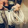 A construction worker holding a coiled bundle of white electrical cable, wearing protective leather gloves and a tool belt. A construction worker holding a coiled bundle of white electrical cable, wearing protective leather gloves and a tool belt.